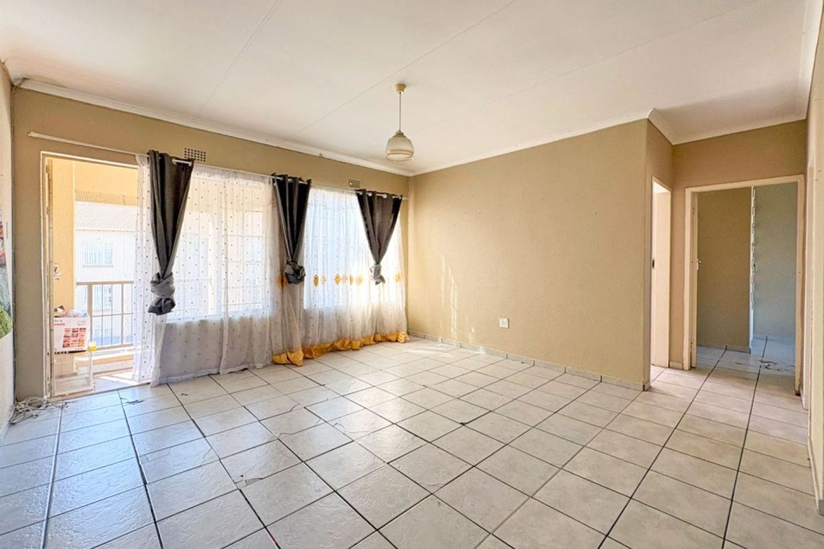 An empty living room featuring tiled flooring, neutral walls, and a sliding glass door providing access to an outdoor balcony area.