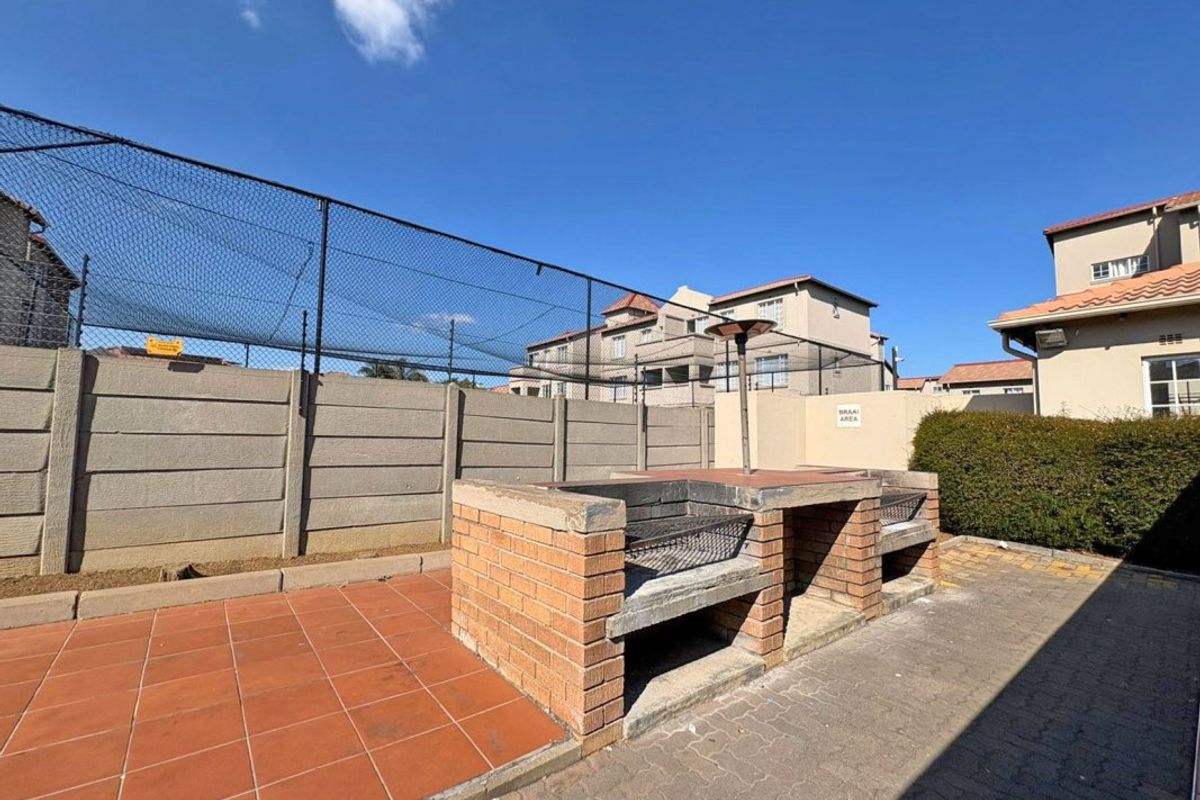 Communal outdoor braai area featuring a built-in brick barbecue, paved flooring, and perimeter security fencing within the apartment complex.