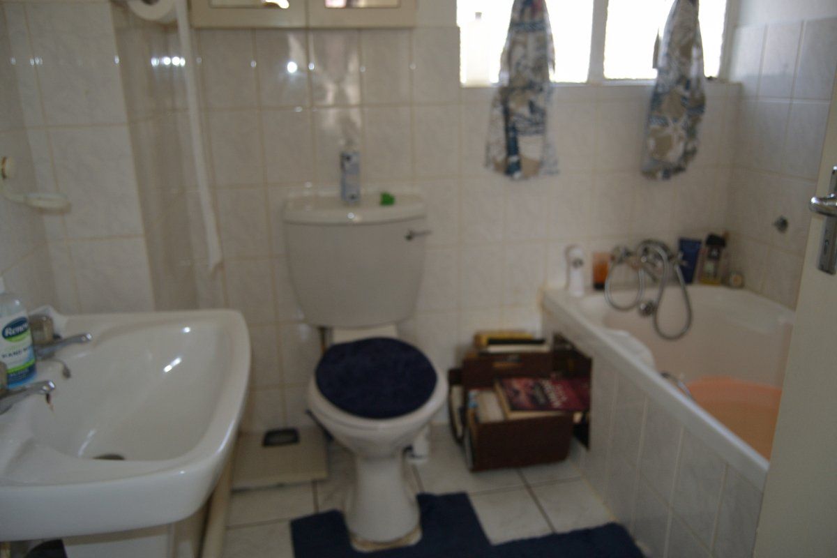 A dated bathroom featuring a pedestal basin, toilet, and bathtub with wall-to-floor tiling, requiring modernization to improve aesthetic appeal and functionality.