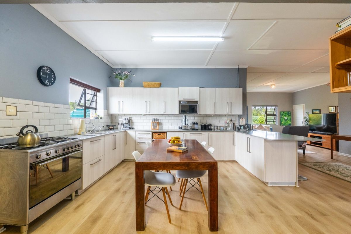 Spacious kitchen featuring light wood-look laminate flooring, white cabinetry, subway tile backsplash, and a functional peninsula, seamlessly flowing into the adjacent living area.