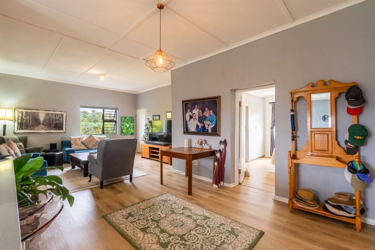 A spacious living room featuring light-toned laminate flooring, a panelled ceiling with pendant lighting, and large casement windows allowing natural light.