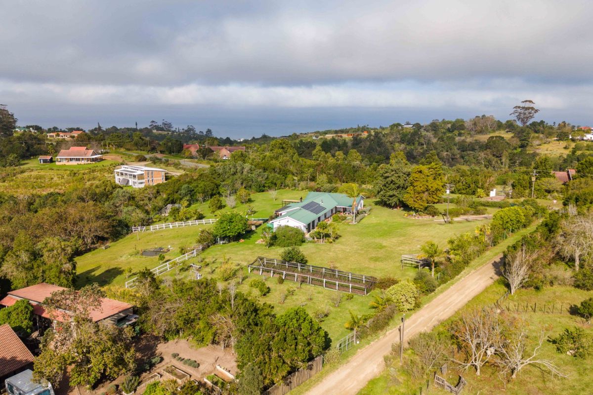 Aerial view of a rural property featuring a house with solar panels, expansive green grounds, and surrounding landscape.