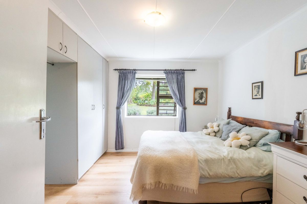 A bright bedroom featuring light laminate flooring, built-in cupboards, and a window overlooking the garden.