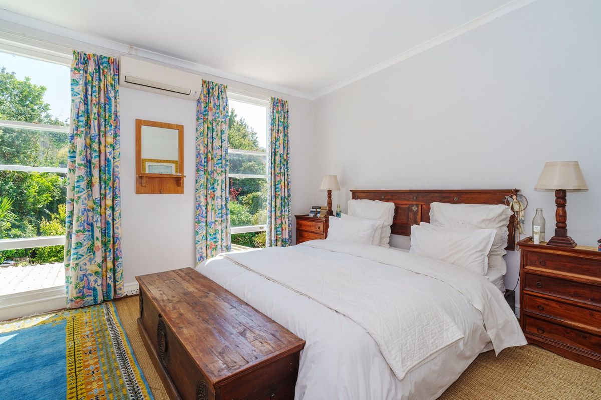 A bright bedroom featuring large windows with garden views, a wall-mounted split-system air conditioner, and classic cornice detailing.