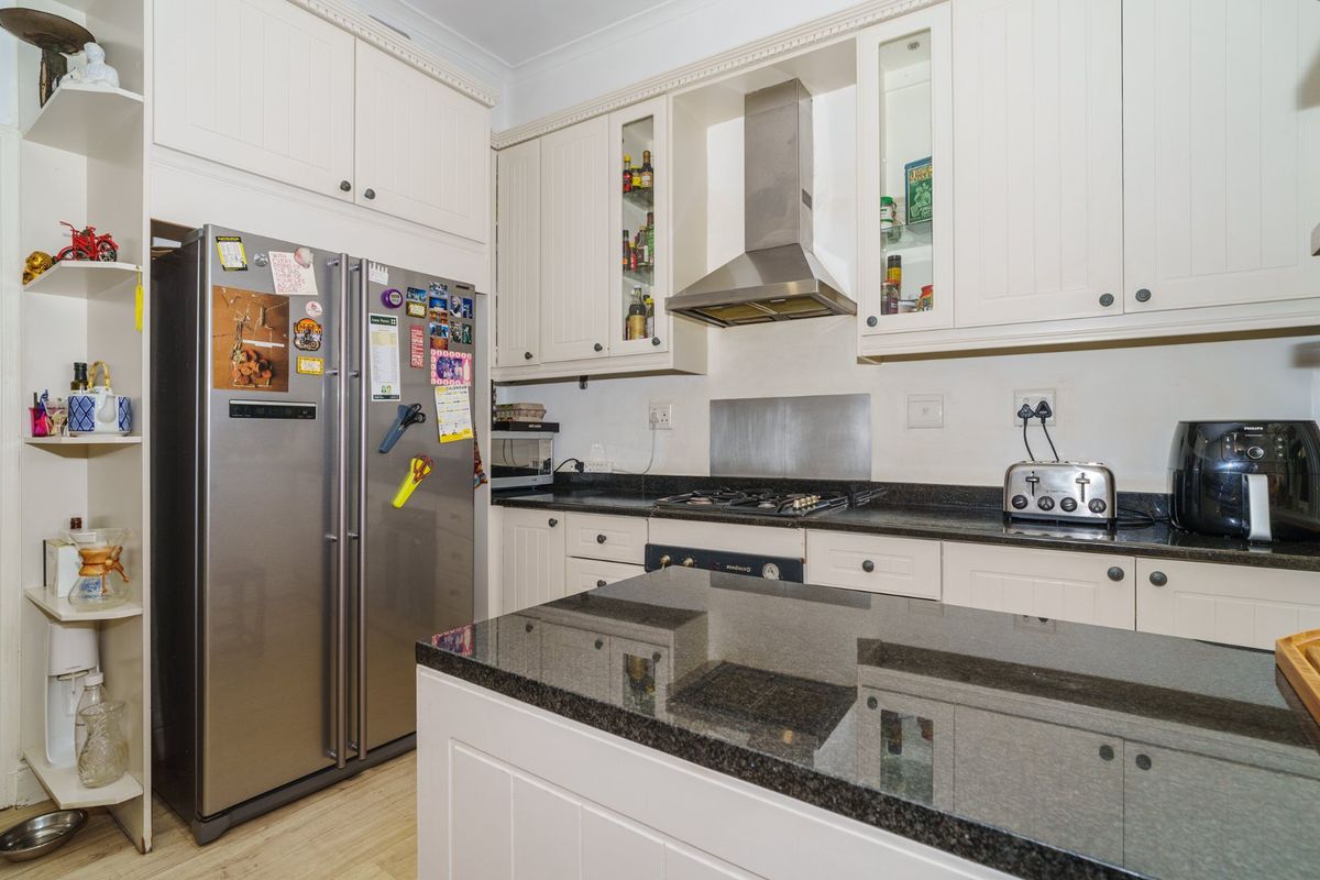 A well-maintained kitchen featuring white cabinetry, granite countertops, a gas hob, and a stainless steel extractor fan with integrated display shelving.