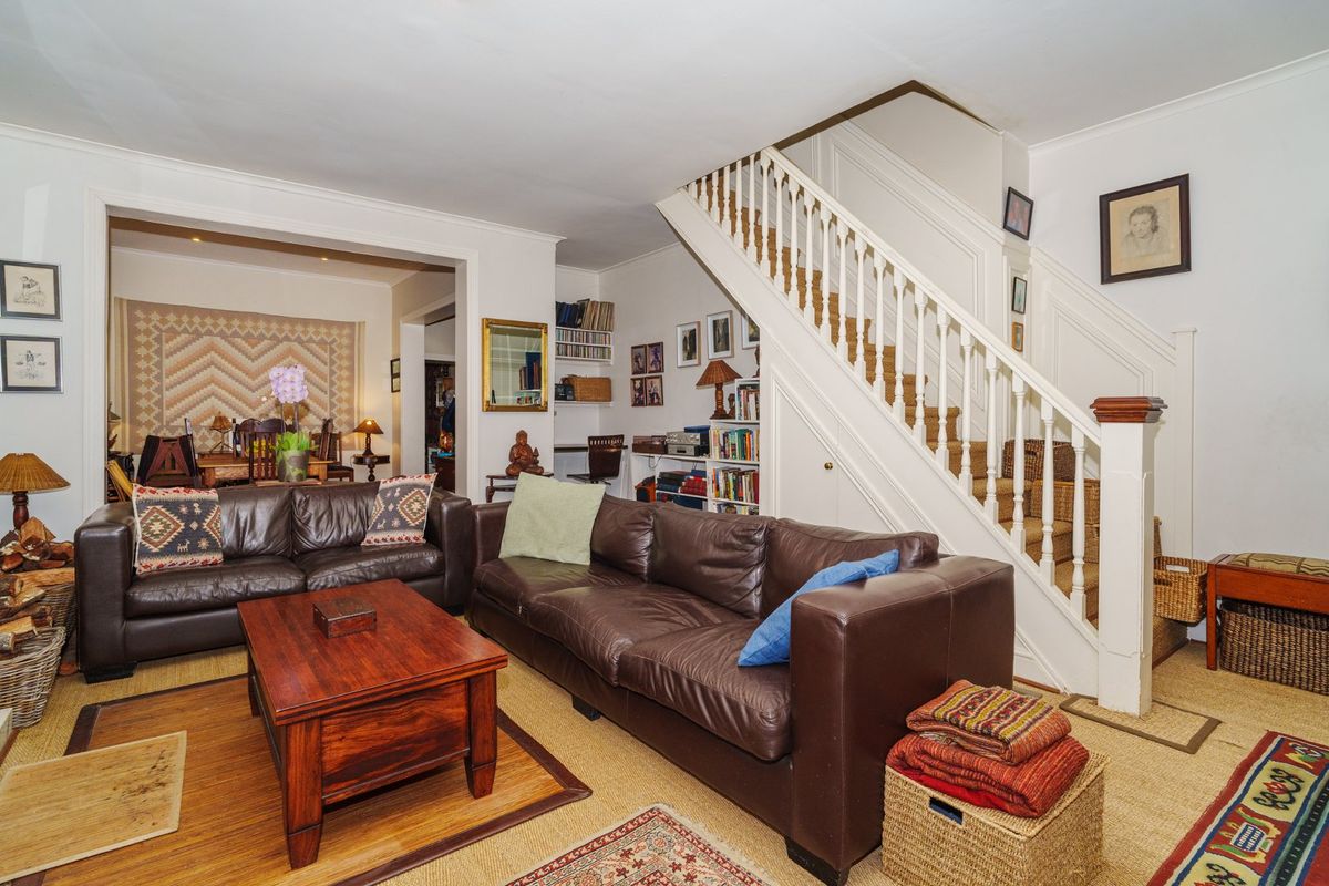 A spacious living room featuring a classic staircase with a wooden balustrade and integrated shelving, leading to an adjacent dining area.
