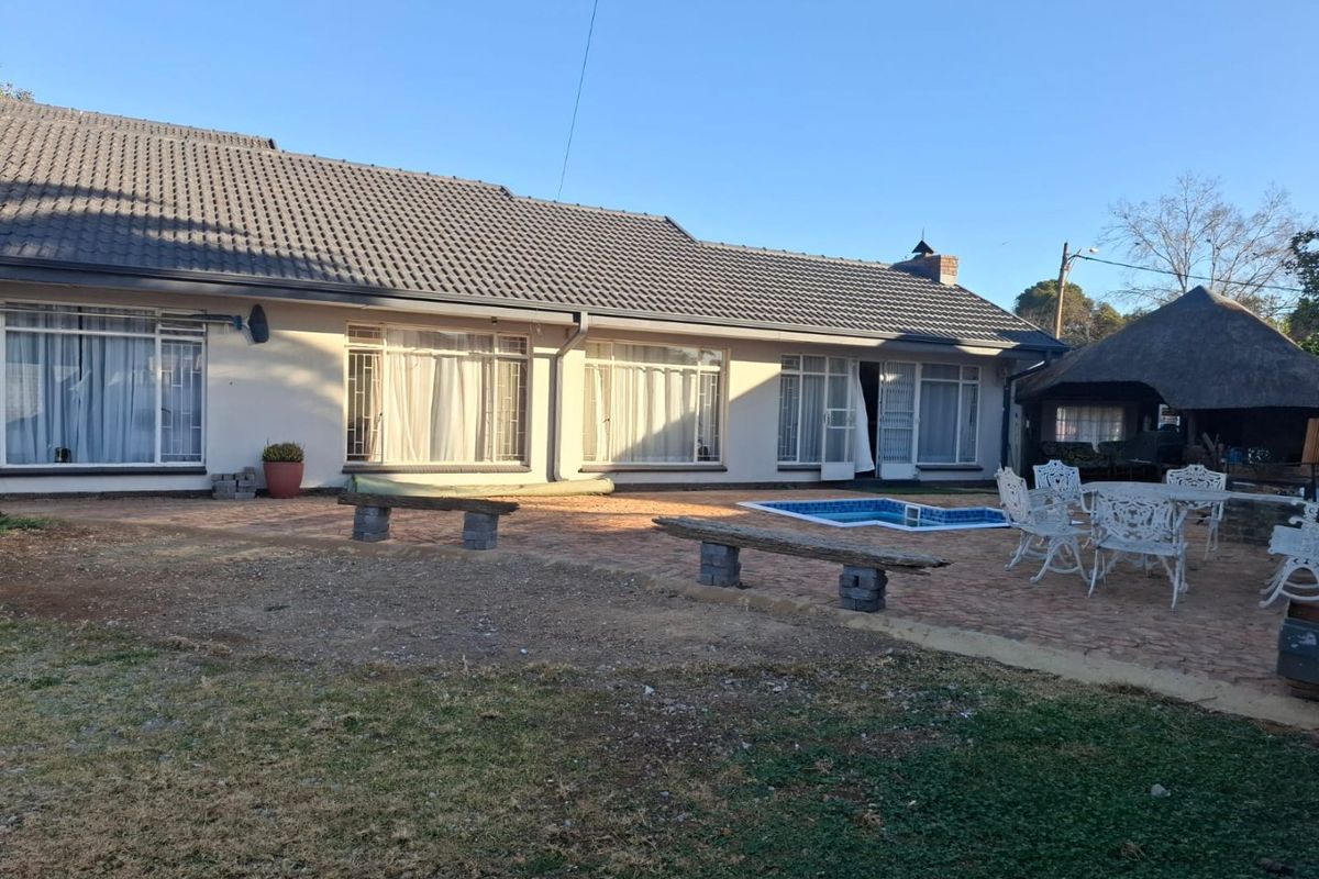 Rear view of the property featuring a paved patio area, a swimming pool, and a thatched lapa structure in the garden.