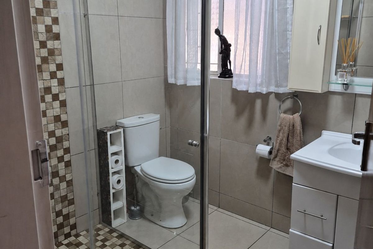 A functional bathroom featuring a glass-enclosed shower with mosaic tile accents, a modern vanity unit, and neutral wall tiling.