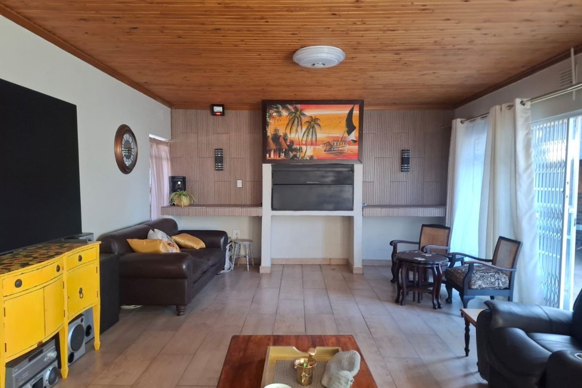 Spacious living room featuring a timber tongue and groove ceiling, tiled flooring, and a central built-in fireplace with sliding door access to the exterior.