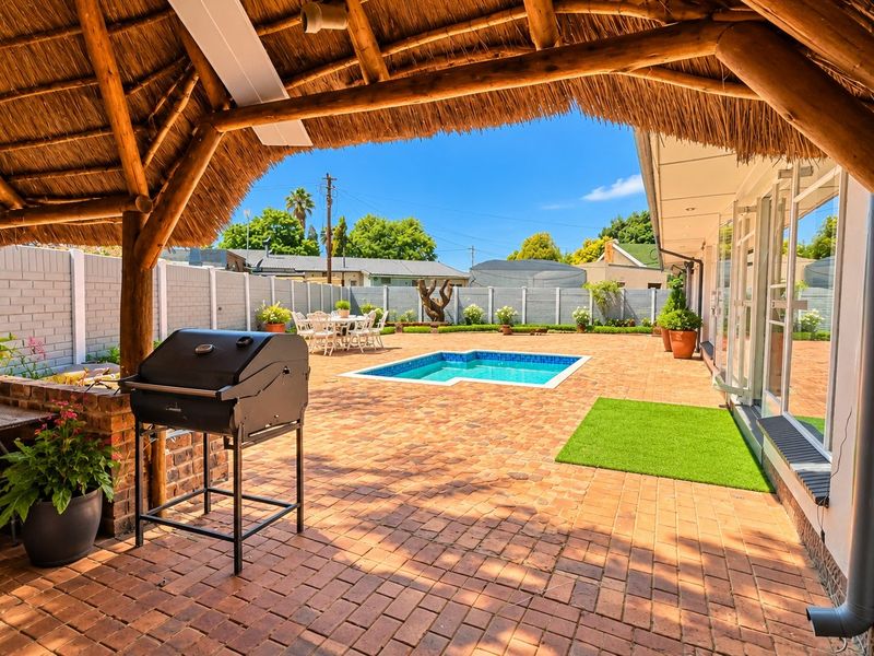 Covered thatched patio area overlooking a paved backyard with a swimming pool and perimeter walling.