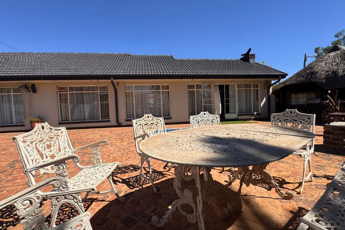 Spacious rear patio area featuring paved flooring, large windows overlooking the garden, and a separate thatched roof structure in the background.