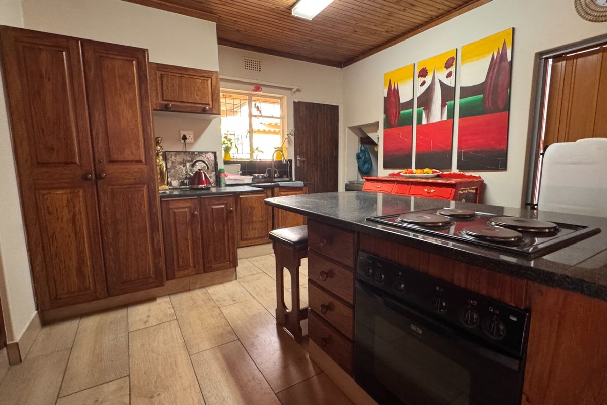 A functional kitchen featuring warm wooden cabinetry, granite countertops, a built-in oven with hob, and a timber-paneled ceiling.