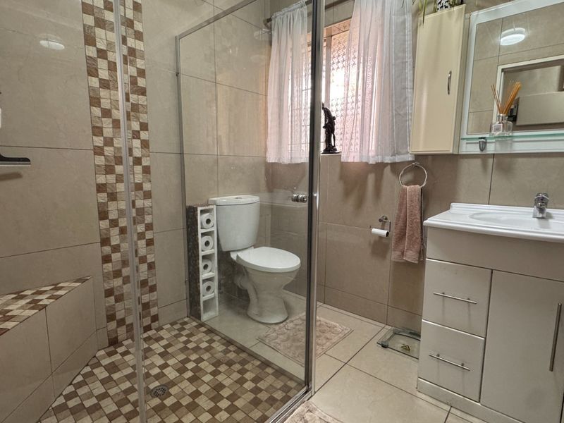 A functional bathroom featuring a glass-enclosed shower, a built-in vanity with a basin, and neutral wall and floor tiling.