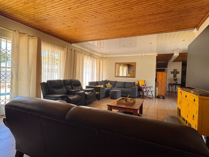 Spacious living room featuring tiled flooring, a timber tongue and groove ceiling, and large sliding glass doors with security gates leading outdoors.