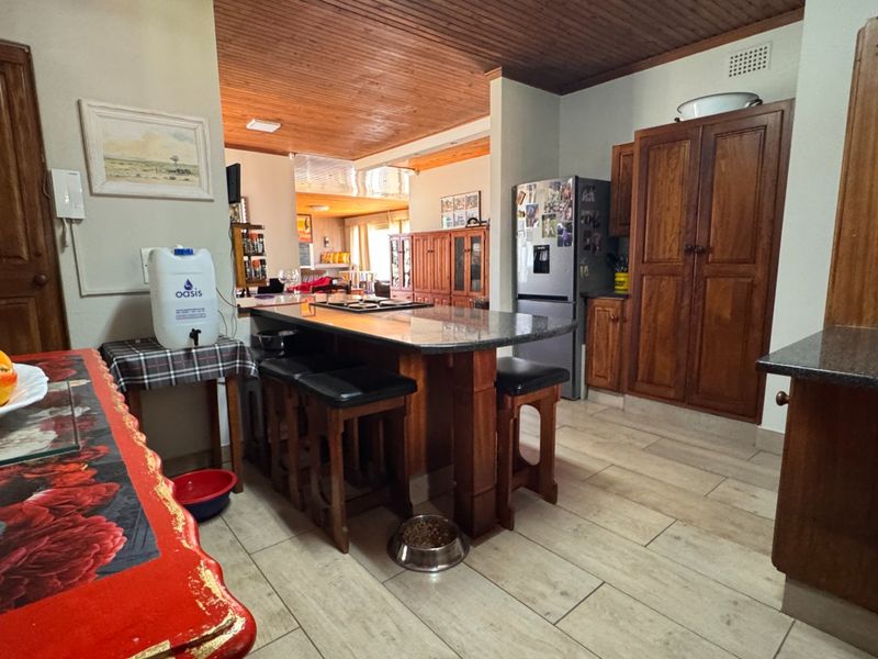 Open plan kitchen and living area featuring wooden cabinetry, granite countertops, a central island, and timber ceiling finishes.