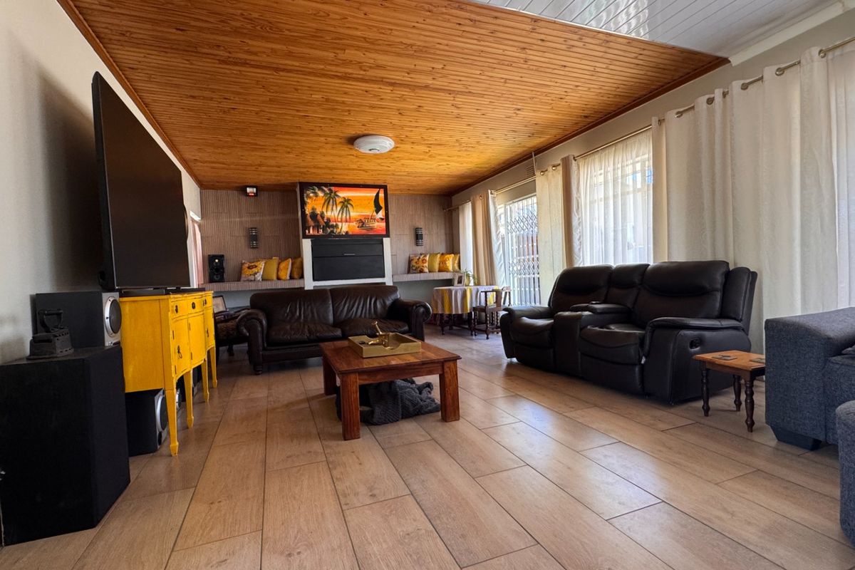 Spacious living room featuring a warm timber-clad ceiling, large format floor tiles, and built-in shelving units.