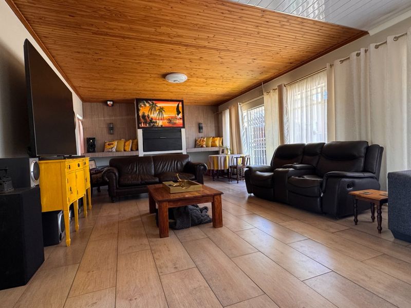 Spacious living room featuring a warm timber-clad ceiling, large format floor tiles, and built-in shelving units.
