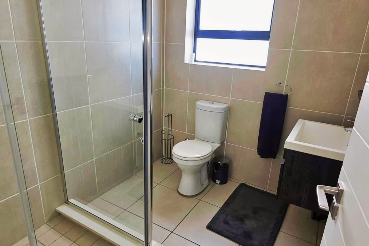 A modern bathroom featuring a glass-enclosed shower, neutral wall and floor tiling, a toilet, and a vanity basin.