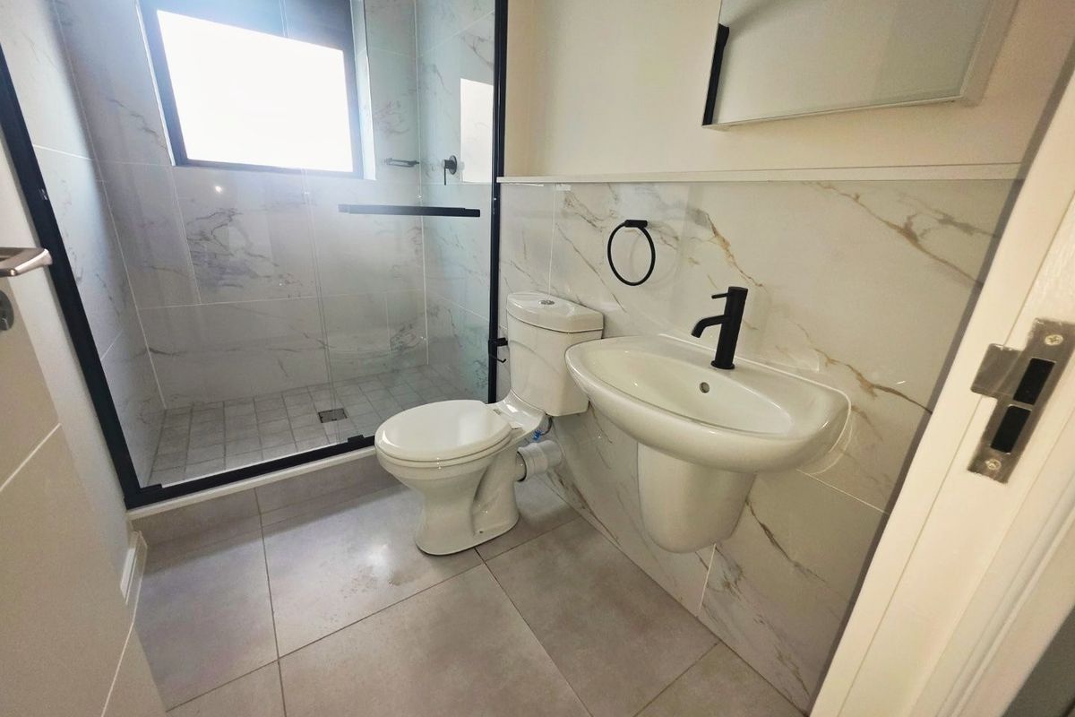 Modern bathroom featuring a walk-in shower with glass screen, pedestal basin, and contemporary marble-effect wall tiling.