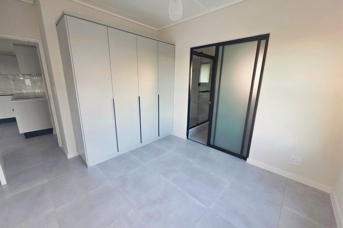 A modern, empty bedroom featuring large-format floor tiles, a sleek built-in wardrobe, and a contemporary sliding glass door leading to an en-suite bathroom.