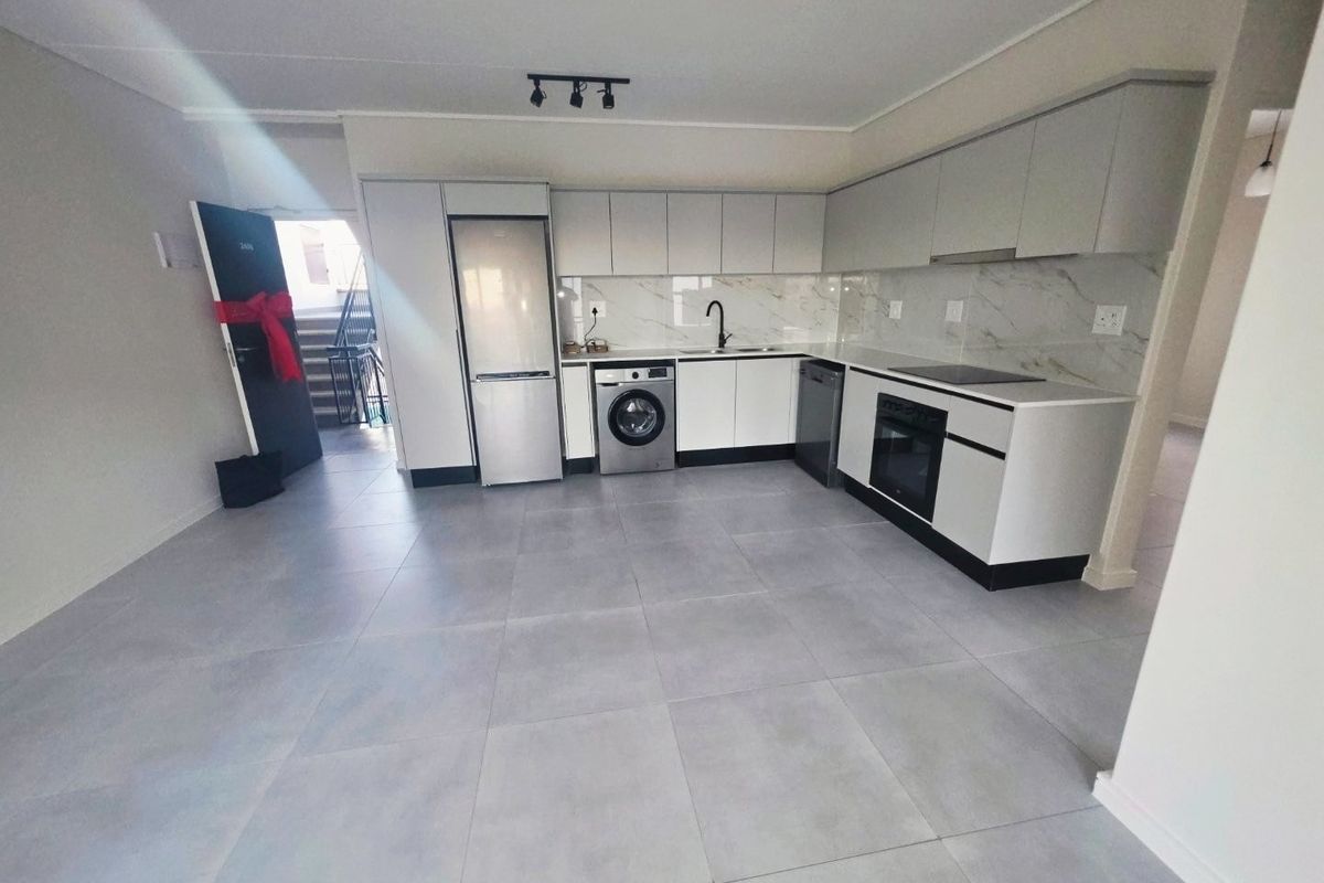 Modern open-plan kitchen featuring sleek cabinetry, marble-look splashback, integrated appliances, and neutral tiled flooring in a clean, contemporary apartment setting.