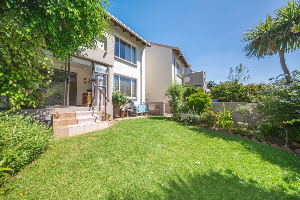 A well-maintained rear garden featuring a lawn, landscaped borders, and a tiled patio area with direct access to the townhouse interior.