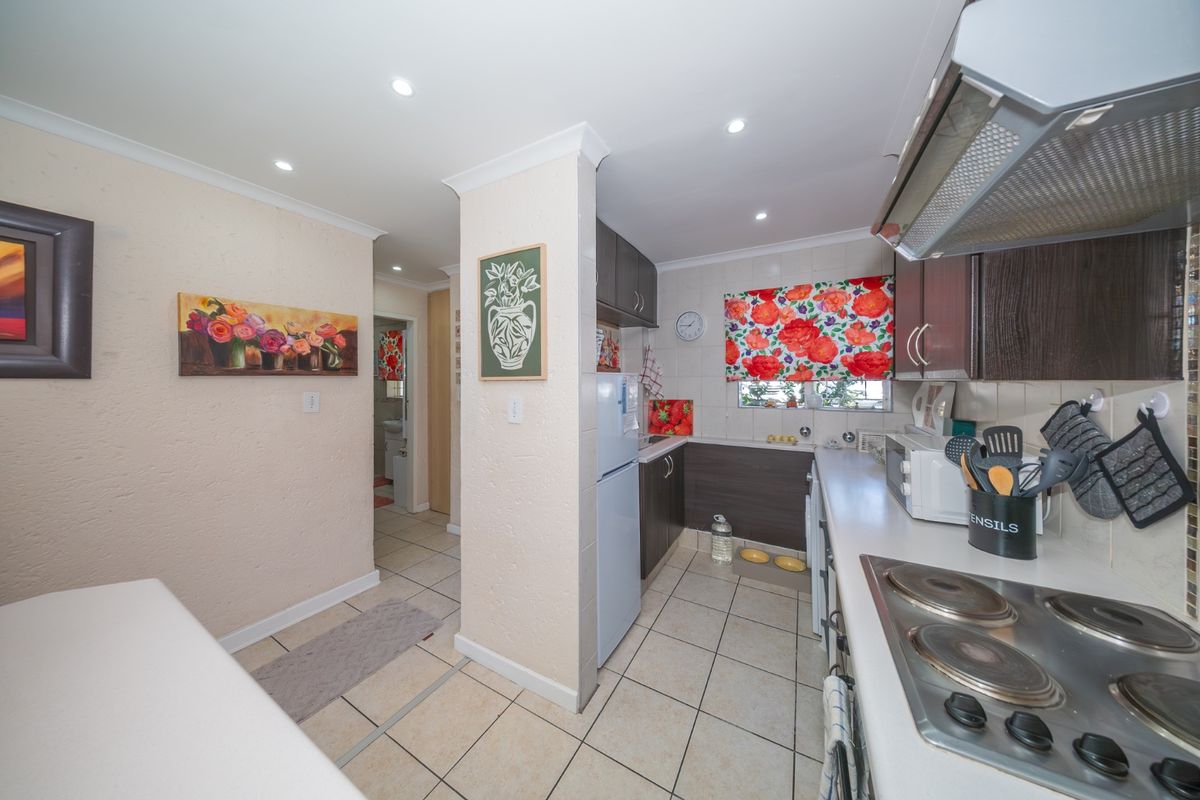 A functional kitchen featuring built-in cabinetry, laminate countertops, an electric hob with extractor fan, and tiled flooring, leading into a hallway area.