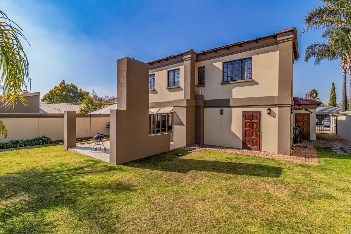 Rear view of the property featuring a landscaped garden, paved patio area with a built-in braai, and access to the home via a timber door.