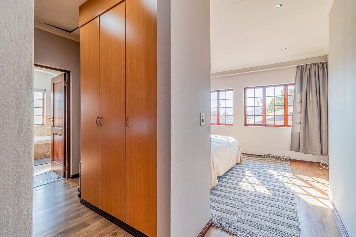 A bright bedroom featuring built-in wooden cupboards, laminate flooring, and large timber-framed windows allowing for ample natural light.