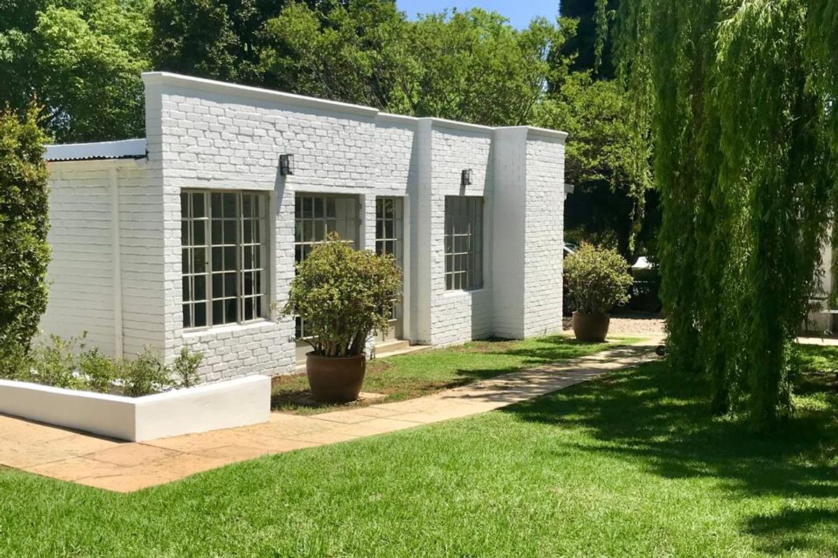 A well-maintained white painted brick exterior featuring steel frame windows, a paved walkway, and a landscaped garden setting.