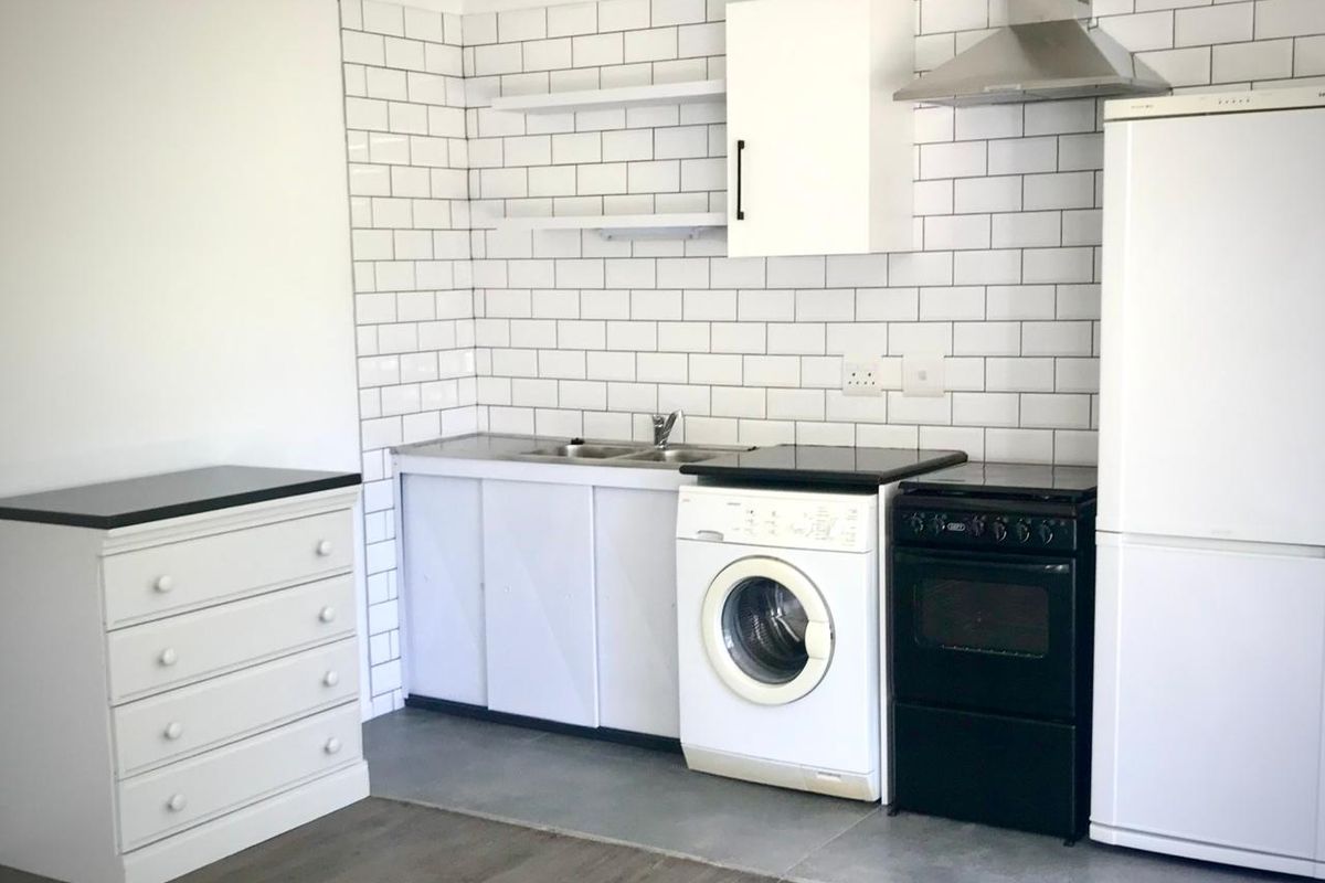 Compact kitchen featuring white subway tile backsplash, stainless steel sink, extractor fan, and functional cabinetry with tiled flooring.
