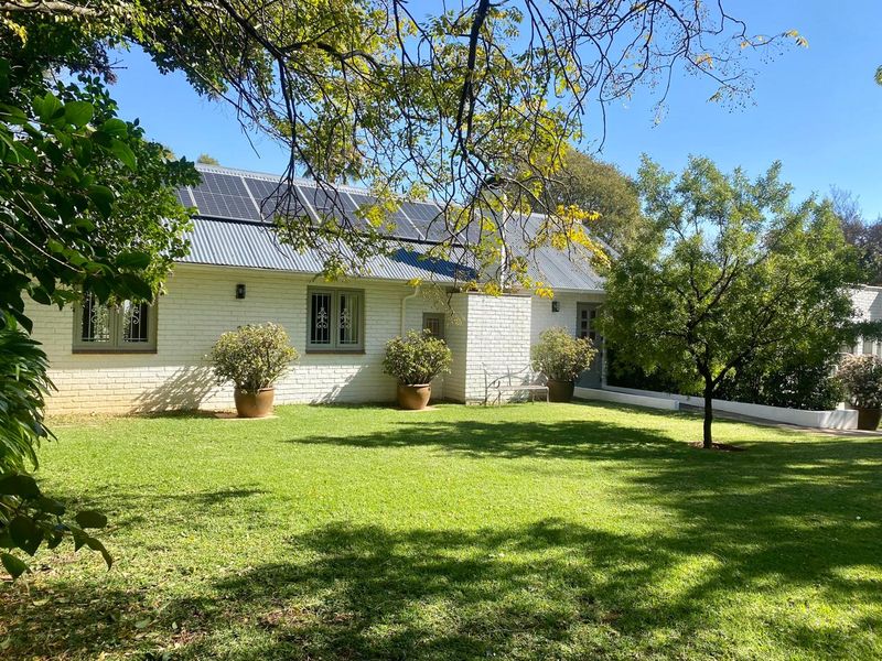A well-maintained rear exterior view of a white brick house featuring a corrugated metal roof equipped with solar panels and a landscaped garden.