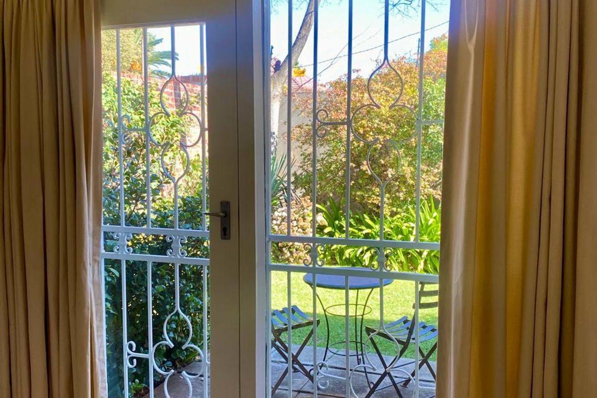 A bright living room area featuring laminate flooring and direct access to a private garden through a secure glass door.