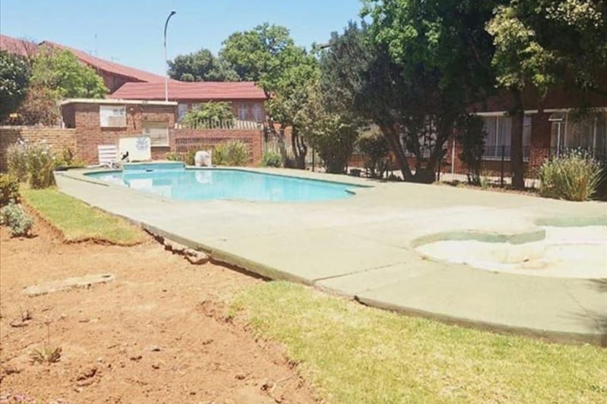Communal swimming pool area featuring a paved surround, brick boundary walls, and surrounding garden space in need of landscaping maintenance.