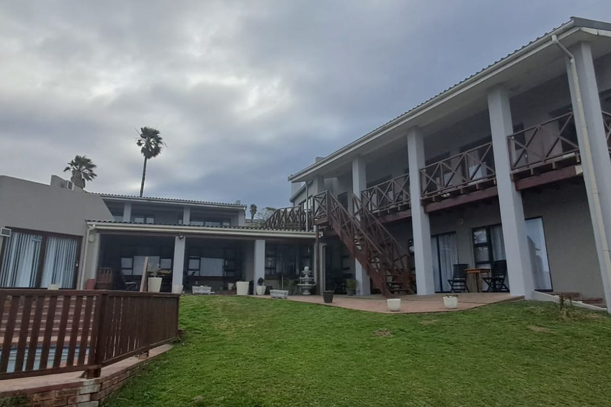 Rear view of a multi-story house featuring a swimming pool, covered patio, upper-level balcony, and external staircase set within a landscaped garden.