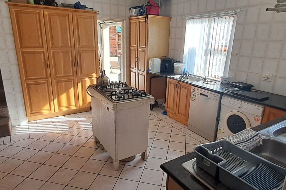 A dated kitchen featuring wooden cabinetry, tiled surfaces, and a central gas hob island, offering significant potential for modernization and layout optimization.