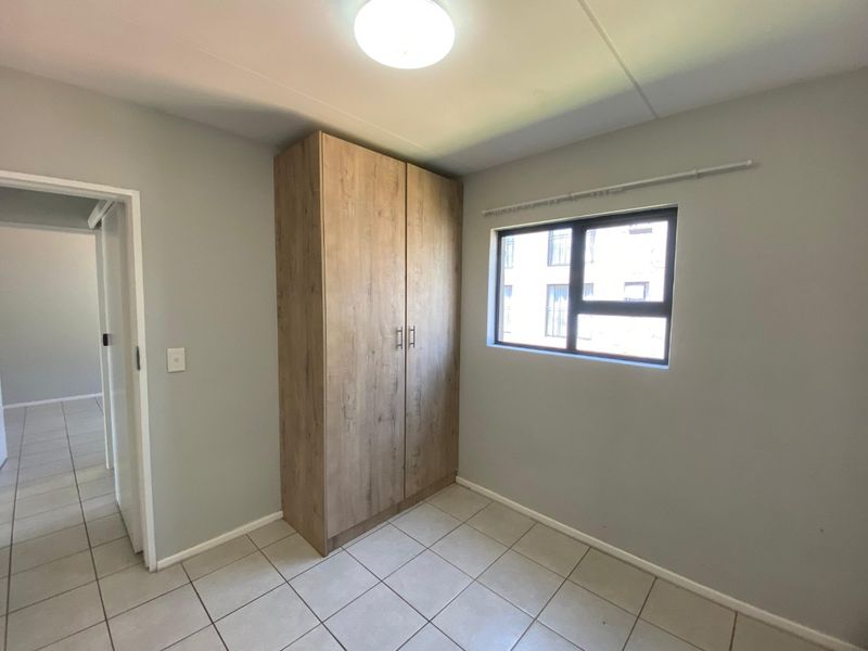 A clean, empty bedroom featuring neutral wall paint, tiled flooring, and a modern wood-finish built-in wardrobe.