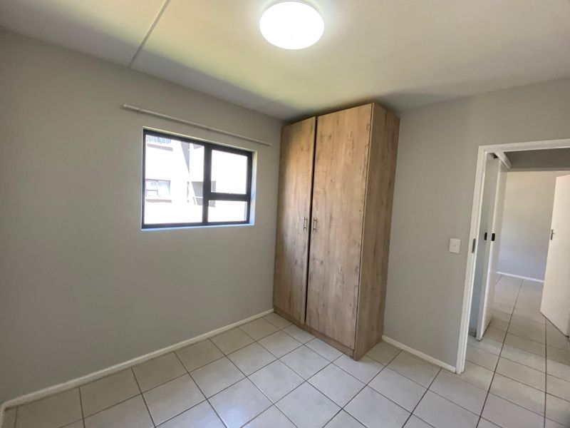 A clean, empty bedroom featuring neutral grey walls, tiled flooring, and a modern wood-finish built-in wardrobe.