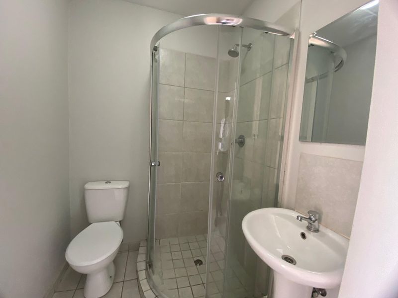 A functional bathroom featuring a curved glass shower enclosure, pedestal basin, and toilet with neutral wall finishes.