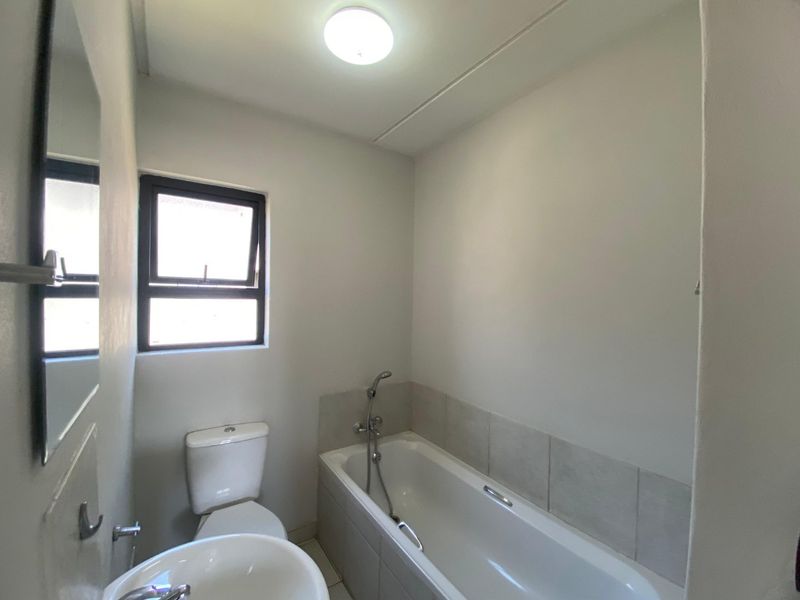 A clean and functional bathroom featuring a bathtub with a handheld shower mixer, a pedestal basin, and a toilet.
