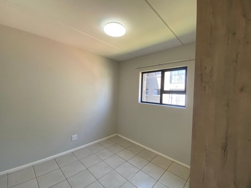 A clean, empty bedroom featuring neutral tiled flooring, a modern aluminium window, and a simple ceiling light fixture.