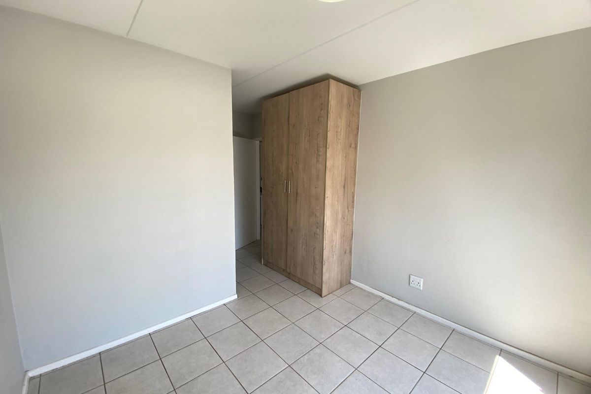 A clean, empty bedroom featuring neutral wall paint, tiled flooring, and a modern wood-finish built-in wardrobe.