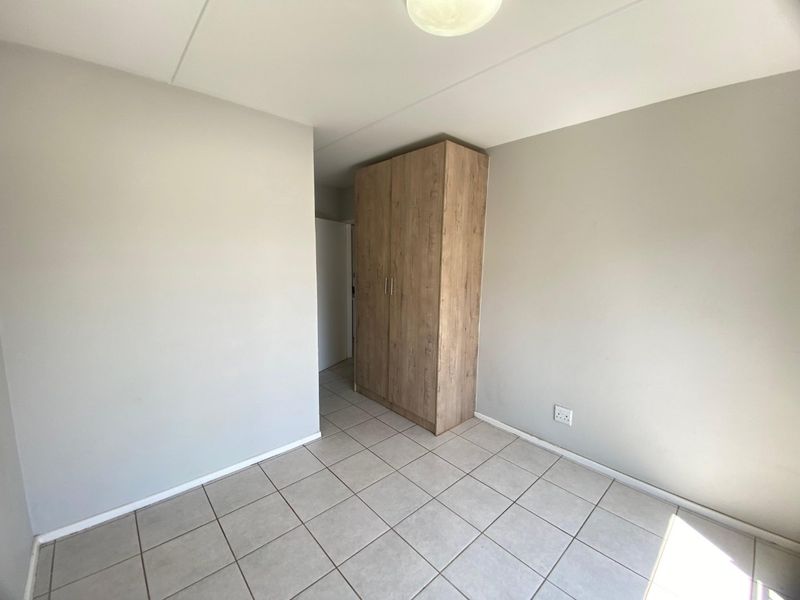 A clean, empty bedroom featuring neutral wall paint, tiled flooring, and a modern wood-finish built-in wardrobe.