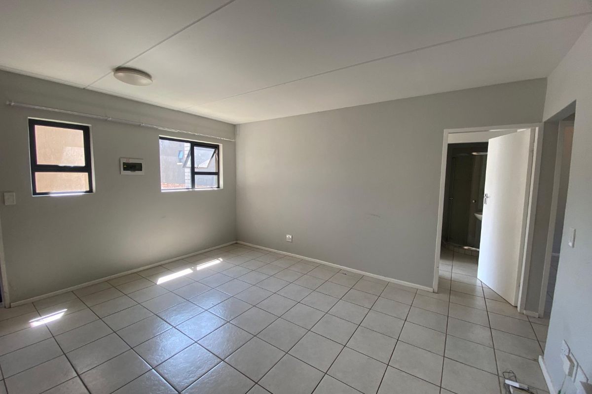 A spacious, empty bedroom featuring neutral tiled flooring, aluminium window frames, and direct access to an adjoining bathroom.