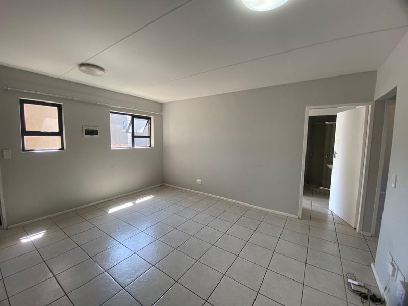 A spacious, empty bedroom featuring neutral tiled flooring, aluminium window frames, and direct access to an adjoining bathroom.
