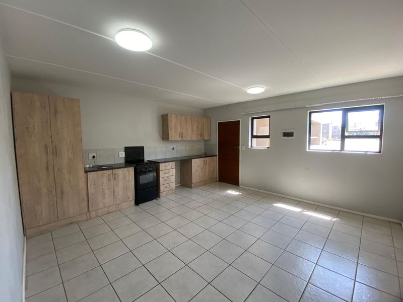 An open-plan kitchen and living area featuring light wood-look cabinetry, tiled flooring, and a functional layout with ample natural light.