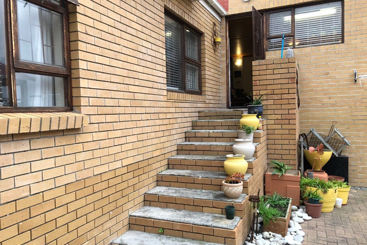 A rear exterior view featuring a brick facade, concrete steps leading to an entrance, and a paved courtyard area.