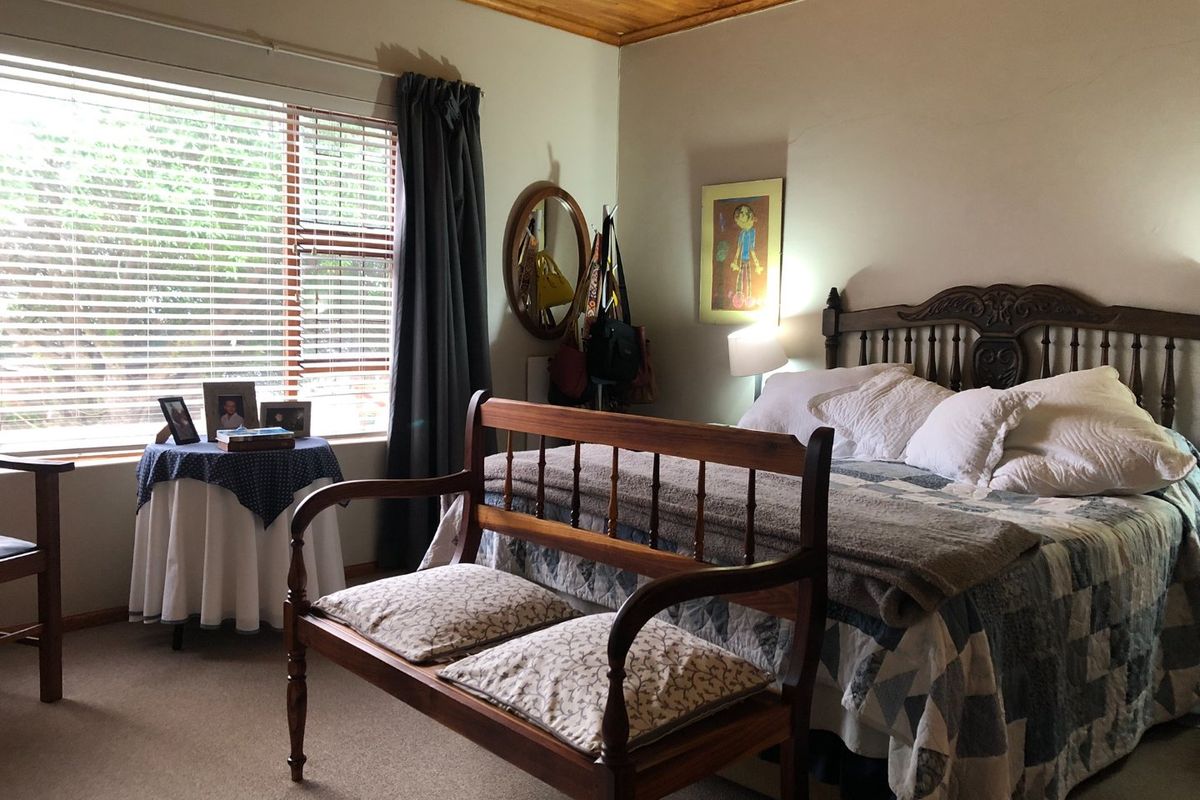 A cozy bedroom featuring a warm timber ceiling and large window with venetian blinds, providing natural light and a comfortable atmosphere.