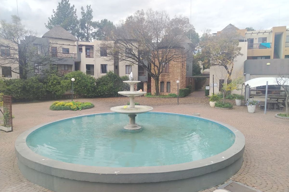 A well-maintained communal courtyard featuring a central water fountain, paved walkways, and landscaped garden areas within the apartment complex.