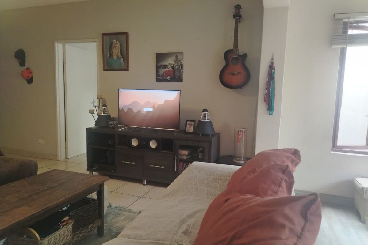 A living room area featuring tiled flooring and a window with fitted blinds, providing a functional space for relaxation.